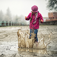 Young girl splashing in muddy puddle