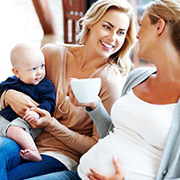 Young woman holding child, sitting next to pregnant woman